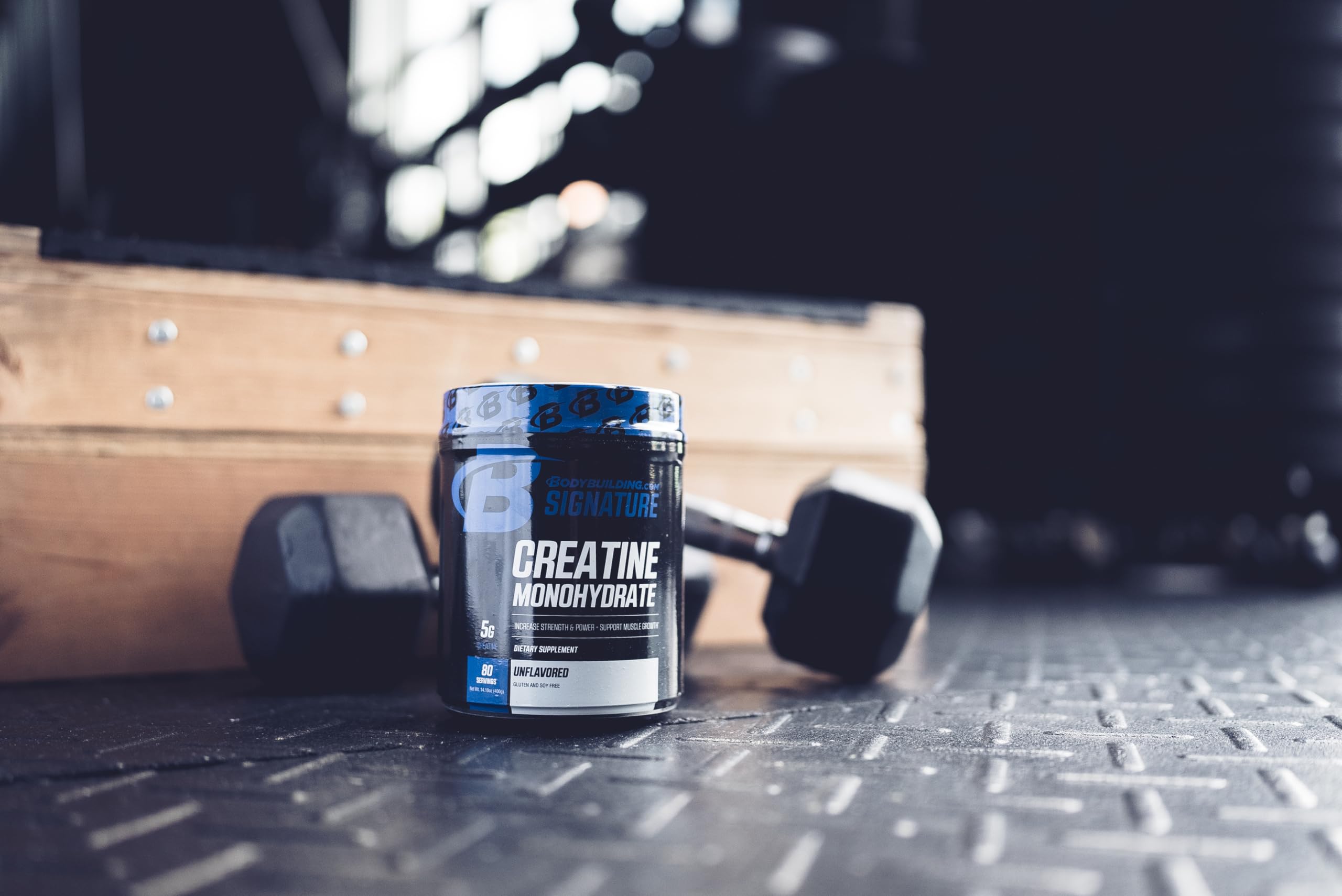 Tub of creatine monohydrate on a gym floor beside dumbbells.